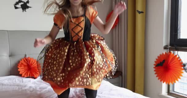 Cute Caucasian little girl with blonde hair seven years old in witch dress and hat having fun and celebrating Halloween at home during Coronavirus covid-19 pandemic and quarantine. Slow motion — Stock Video