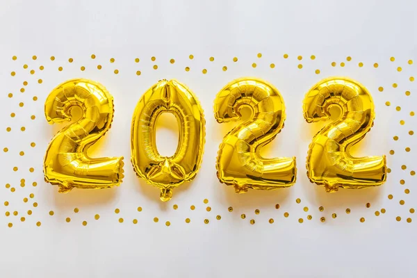 Happy new year 2022 background. Metallic balloons golden color on white with confetti. Flat lay, top view, mockup, overhead. Winter holiday celebration