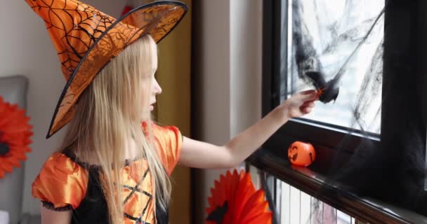 Söt vit liten flicka med blont hår sju år gammal i häxa klänning och hatt har roligt och firar Halloween hemma under Coronavirus covid-19 pandemi och karantän. Långsamma rörelser — Stockvideo