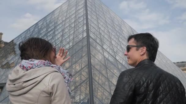 Счастливая пара стоит рядом с пирамидой у входа в музей Лувра — стоковое видео