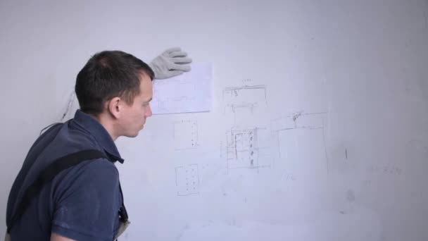Hombre constructor compara esquema en la pared y plan de renovación — Vídeos de Stock