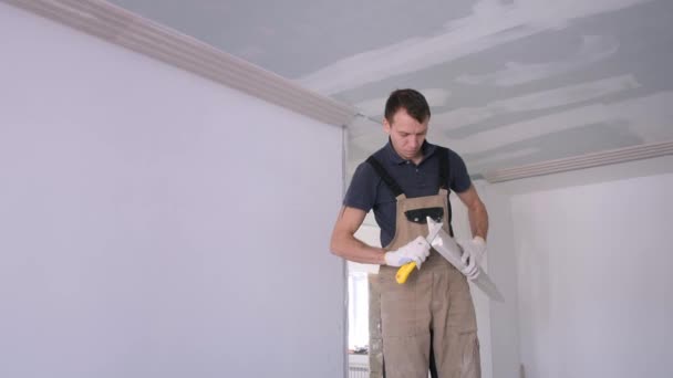 Мужчина строитель шлифует штукатурку лаком с ножом в квартире — стоковое видео