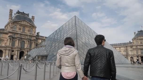 Pareja recién casada camina uniendo sus manos a la pirámide cerca del Louvre — Vídeos de Stock