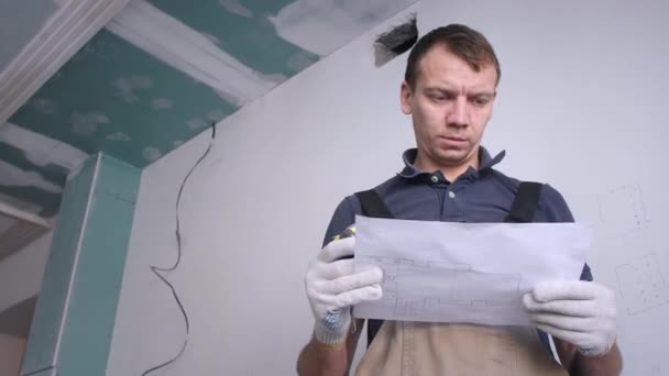 Ο μάστορας με τη φόρμα κοιτάζει το σχέδιο ανακαίνισης σε χαρτί — Αρχείο Βίντεο