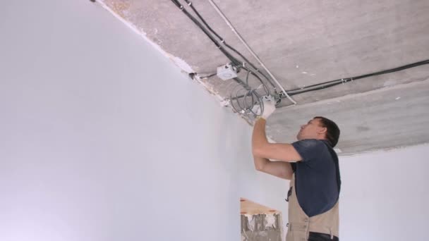 Hombre trabajador en chándal instala caja de conexiones eléctricas — Vídeos de Stock