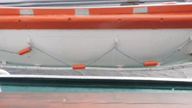 Turuncu ve beyaz yedek tekne gemi korkuluklarının yanında asılı.