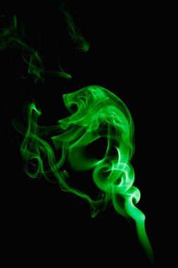 Esrarengiz bukleler ve koyu arkaplanda yeşil duman şekilleri. Yanan bir tütsü çubuğundan yükselen duman.