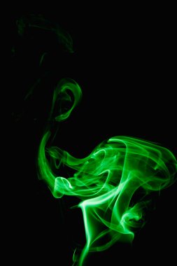 Esrarengiz bukleler ve koyu arkaplanda yeşil duman şekilleri. Yanan bir tütsü çubuğundan yükselen duman.