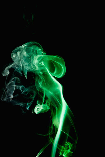 Whimsical curls and shapes of green smoke on a dark background. Streaming smoke from a burning incense stick.