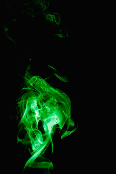 Whimsical curls and shapes of green smoke on a dark background. Streaming smoke from a burning incense stick.