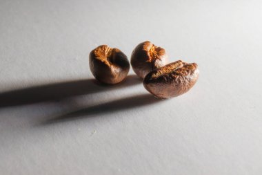 Yakından kavrulmuş aromatik kahve taneleri. Otlak ışığında beyaz kağıt üzerinde kahve taneleri. Kahve çekirdeklerinden uzun gölgeler. Kağıt dokusu.
