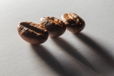 Yakından kavrulmuş aromatik kahve taneleri. Otlak ışığında beyaz kağıt üzerinde kahve taneleri. Kahve çekirdeklerinden uzun gölgeler. Kağıt dokusu.