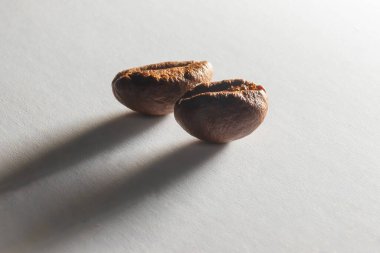 Yakından kavrulmuş aromatik kahve taneleri. Otlak ışığında beyaz kağıt üzerinde kahve taneleri. Kahve çekirdeklerinden uzun gölgeler. Kağıt dokusu.