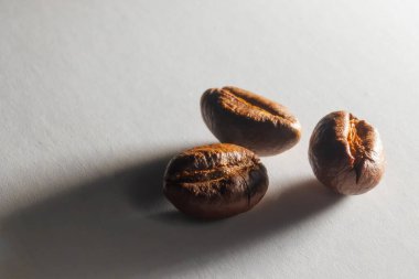 Yakından kavrulmuş aromatik kahve taneleri. Otlak ışığında beyaz kağıt üzerinde kahve taneleri. Kahve çekirdeklerinden uzun gölgeler. Kağıt dokusu.