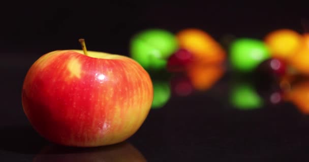 Natural red and yellow apple against the background of artificial fruits and berries on the table. — Stock Video