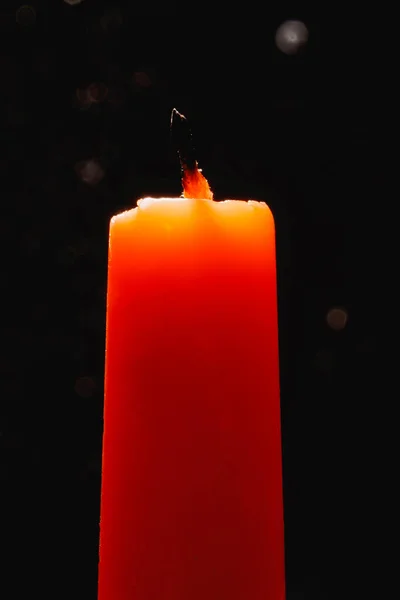 Uma vela laranja extinta contra um fundo escuro na luz de fundo. — Fotografia de Stock