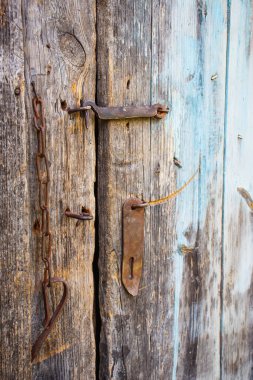 En basit kırsal kapı kilidi. Eski bir kırsal binanın ahşap kapısında paslı bir asma kilit. Kırık tahtalar güneşte yanmış..