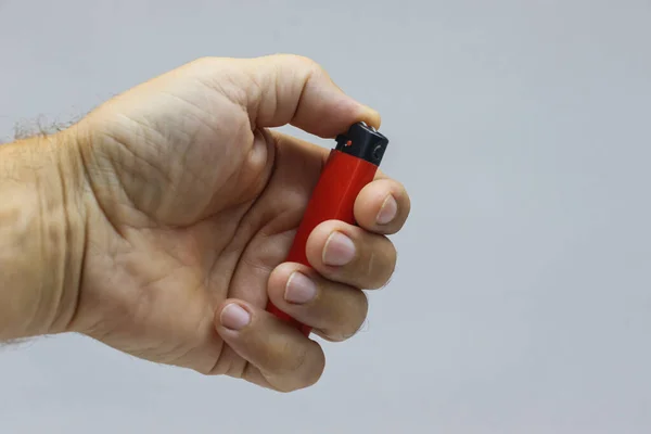 Un briquet rouge dans sa main gros plan sur un fond clair. — Photo