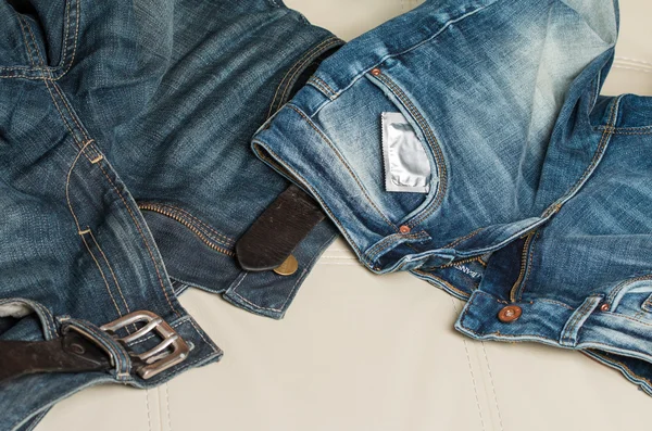 A condom and a pair of jeans on the couch — Stock Photo, Image