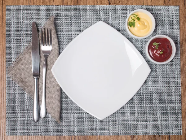 Пустая тарелка с вилкой и ножом, кетчупом и майонезом — стоковое фото