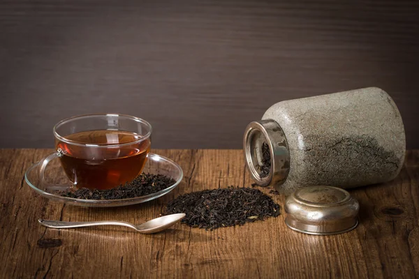 Scattered dry tea leaves with glass cup of tea — Stock Photo, Image