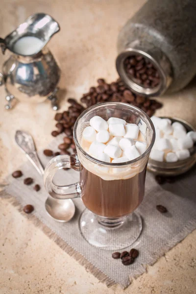 Скляна чашка кави з зефіром, молочним глечиком та кавовими зернами — стокове фото