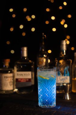 Mavi Long Island Elektrik Kokteyli Bardakta ve arka planda şişeler