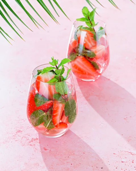 Summer mint and strawberry infused water on pink table top with long shadows, top view