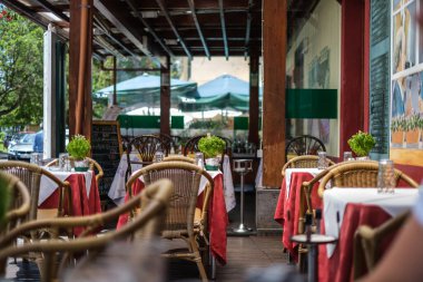 Boş bir balkon, öğle yemeği için misafir kabul etmeye hazır masalar, kırmızı perdeler ve teneke sandalyeler Madeira, Portekiz 'de güneşli bir günde