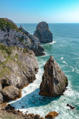 Dağın yakınındaki okyanusta kayalar berrak mavi gökyüzünde güçlü ve heybetli.