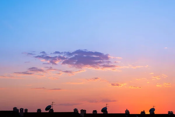 Güneşin alacakaranlıktaki parlak renkleri gökyüzündeki bir buluta yansıyor. Birbiri ardına evlerin siluetiyle birlikte.