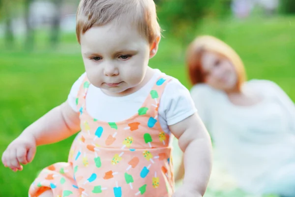 independent child, first steps, under the supervision of the mother, maternal care, family idyll, family vacation in the park on the lawn, summer vacation, walk with a toddler, the child grows