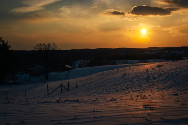 雪に覆われたなだらかな丘とキャロルの農地に沈む夕日 — ストック写真