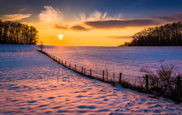 Puesta de sol sobre una valla en un campo cubierto de nieve en Carrol rural — Foto de Stock