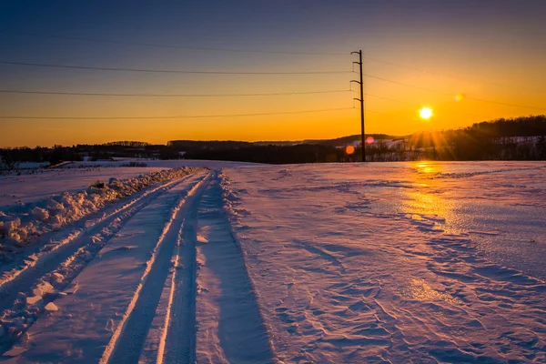 Pôr do sol sobre uma estrada de terra coberta de neve no condado rural de York, Penns — Fotografia de Stock