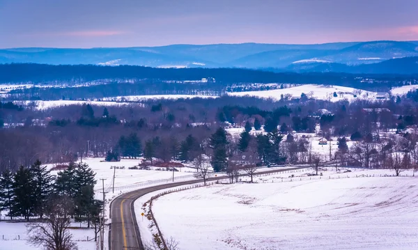 View of road through snow-covered fields and distant mountains, — Stock Photo, Image