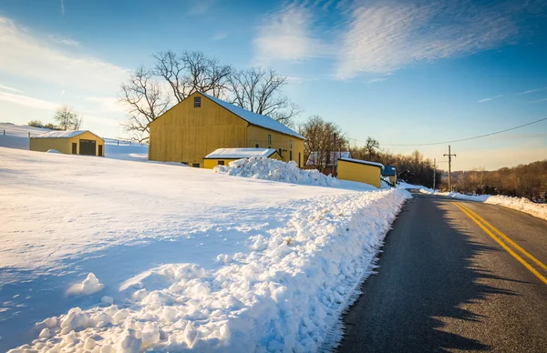 Granero amarillo y un campo cubierto de nieve a lo largo de un camino rural en Yor — Foto de Stock