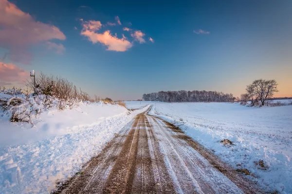 Salju menutupi lapangan sepanjang jalan tanah saat matahari terbenam, di pedesaan York Co — Stok Foto