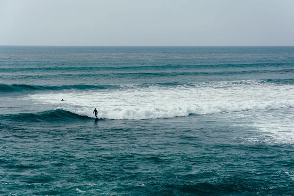 Dalgalar ve sörfçü Pasifik Okyanusu günbatımı kayalıklarla doğal p — Stok fotoğraf