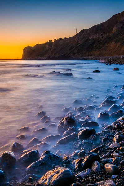 Lange Belichtungszeit von Wellen, die bei Sonnenuntergang auf Felsen krachen, aufgenommen bei pel — Stockfoto