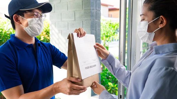 Asian deliver man wearing face mask in uniform handling bag of food and fruit give to woman costumer in front of the house, Express delivery service quarantine and shopping concept