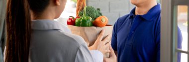 Kapıdaki müşteriye yiyecek ve sebze dolu çanta taşıyan Asyalı teslimatçı. Yemek teslimatı konsepti.