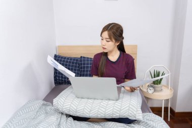 Yatakta dizüstü bilgisayar kullanan Asyalı kadın evde çalışmaktan, uzaktan çalışmaktan ya da evden çalışmaktan keyif alıyor..