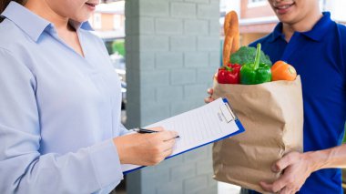 Kapıdaki müşteriye yiyecek ve sebze dolu çanta taşıyan Asyalı teslimatçı. Yemek teslimatı konsepti.