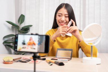 Güzel Asyalı kadın blogcu video kaydını kullanarak canlı yayın yapıyor ve evdeki kozmetikler için makyaj yapıyor..