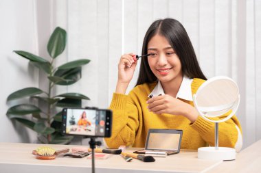 Güzel Asyalı kadın blogcu video kaydını kullanarak canlı yayın yapıyor ve evdeki kozmetikler için makyaj yapıyor..
