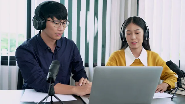 Asian woman radio hosts gesturing to microphone while interviewing a man guest in radio station during a show for radio live in the Studio