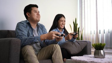 Heyecanlı genç çift video oyunları oynuyorlar. Oyun kontrolörleri kanepeye oturup geceleri evlerinde yeni teknoloji konsollarıyla eğleniyorlar..