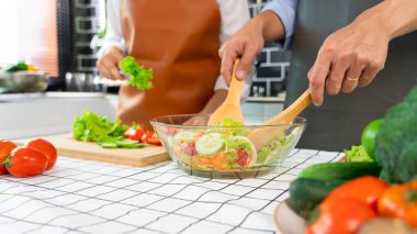 Mutlu çift evde mutfakta dikilip sebze salatası hazırlarken karı koca vejetaryenler sebzeleri doğrarken evde mutfak hazırlarken eğleniyor.