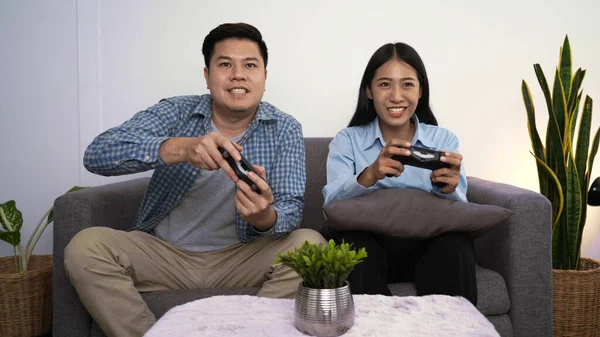 夜に自宅で新しい技術コンソールをオンラインで楽しんでソファの上に座ってゲームコントローラを保持しているビデオゲームをプレイして興奮面白い若いカップル — ストック写真